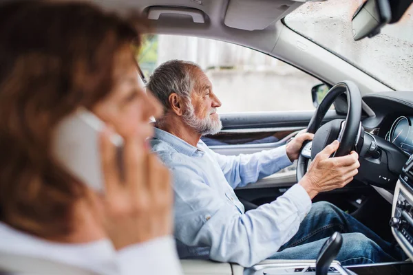 Feliz pareja de ancianos con teléfono inteligente sentado en el coche, hablando . — Foto de Stock