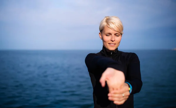 Porträt einer jungen Sportlerin, die draußen am Strand sitzt und sich streckt. — Stockfoto