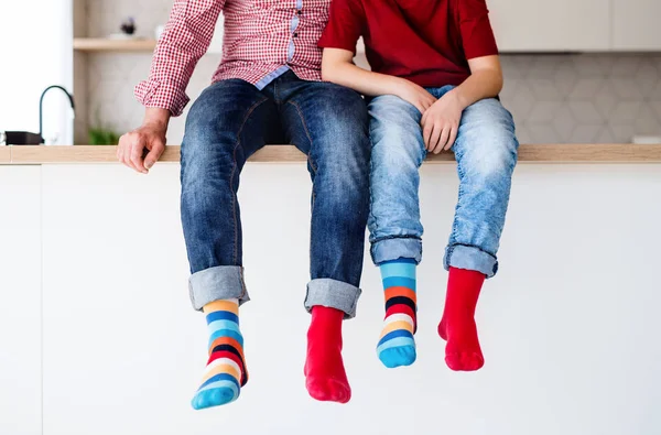 Midsection of father with son with funky socks sitting on kitchen counter indoors. — Stock Photo, Image