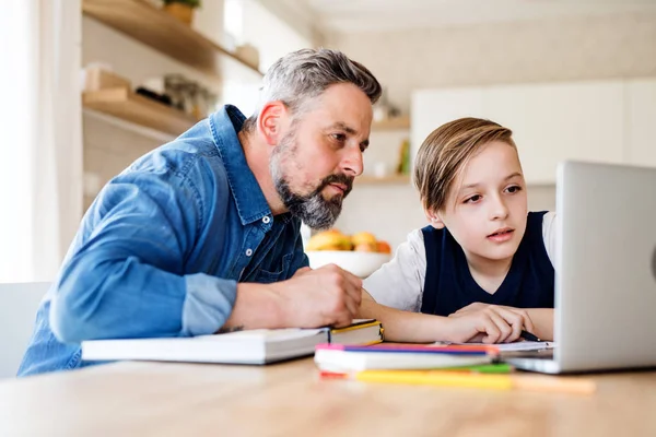 Volwassen vader met kleine zoon zittend aan tafel binnenshuis, met behulp van laptop. — Stockfoto