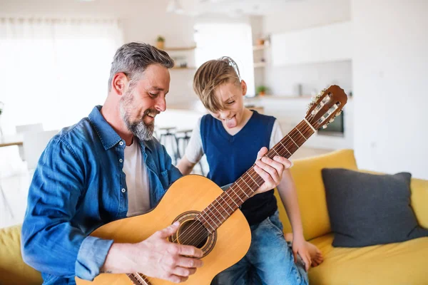 Küçük oğlu ile olgun baba kanepede kapalı oturan, gitar çalıyor. — Stok fotoğraf