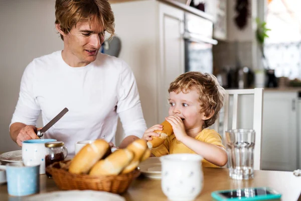 Giovane padre con un figlio bambino che fa colazione al chiuso a casa . — Foto Stock