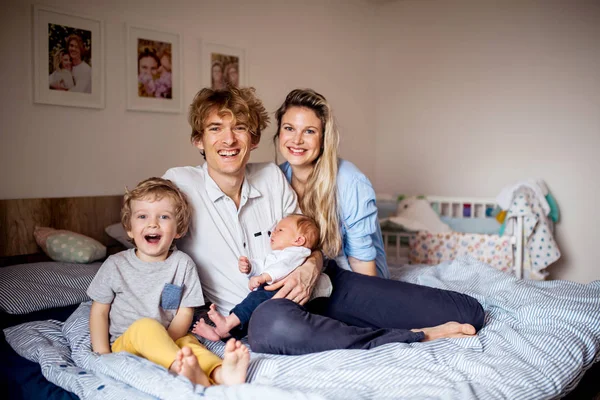 Young parents with newborn baby and small toddler son at home. — Stock Photo, Image