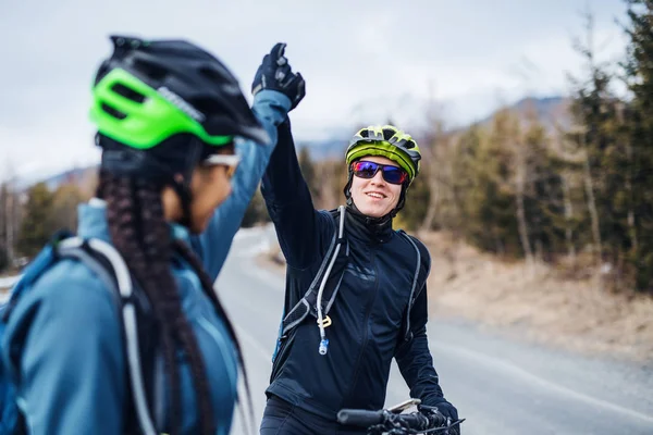 Dos ciclistas de montaña de pie en la carretera al aire libre en invierno, dando cinco . — Foto de Stock