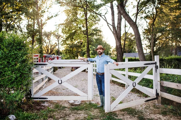 A portrait of farmer walking outdoors on family farm, opening gate. — Stock Photo, Image