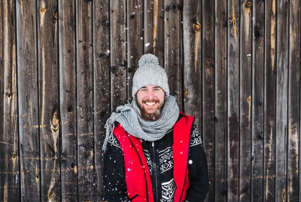 Junger Mann steht im Winter draußen vor hölzernem Hintergrund. — Stockfoto