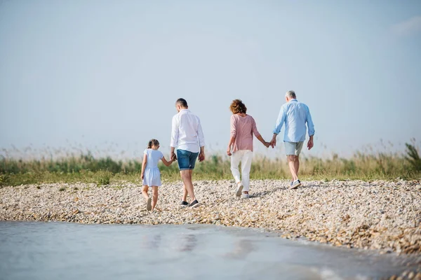 Η πίσω όψη της οικογένειας πολλών γενεών σε διακοπές με τα πόδια δίπλα στη λίμνη, που λειτουργεί. — Φωτογραφία Αρχείου