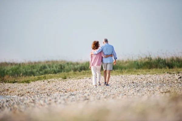 Blick von hinten auf ein älteres Ehepaar im Urlaub bei einem Spaziergang am See,. — Stockfoto