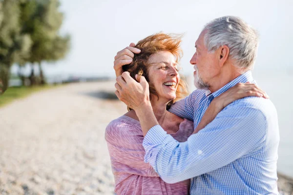 Coppia anziana in vacanza passeggiando lungo il lago, abbracciandosi . — Foto Stock