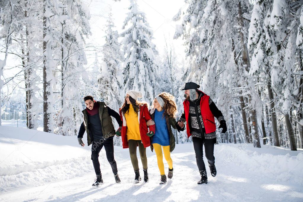 A group of young friends on a walk outdoors in snow in winter forest.