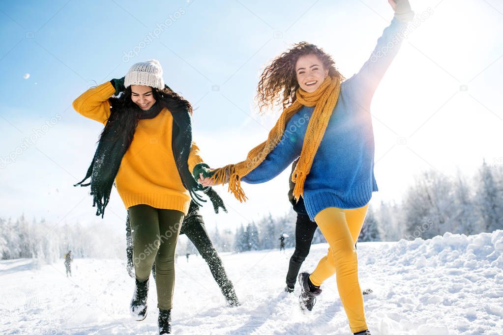 A group of young friends on a walk outdoors in snow in winter forest, running.