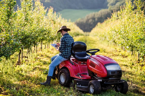 Взрослый фермер с табличкой, стоящей у мини-трактора на открытом воздухе в саду . — стоковое фото