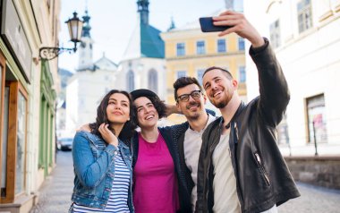 Şehirde dışarıda duran bir grup genç arkadaş selfie çekiyor.