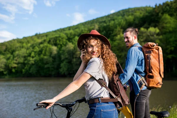 Pareja de turistas jóvenes con scooters eléctricos en la naturaleza, de pie junto al lago . — Foto de Stock