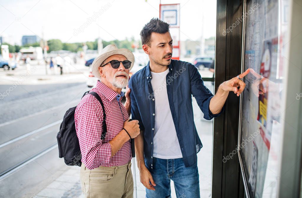 Young man and blind senior with white cane at bus stop in city.