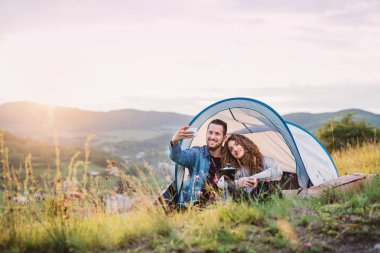 Genç turist çift doğada oturan çadır barınak ile gezginler, selfie alarak.