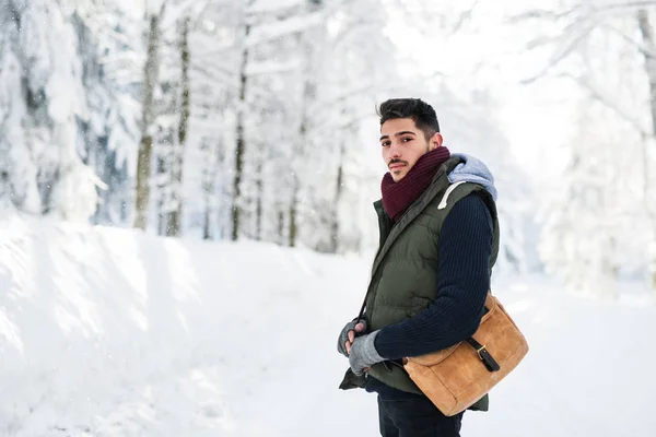 Kış ormanında karda dışarıda duran genç adam, kameraya bakıyor. — Stok fotoğraf