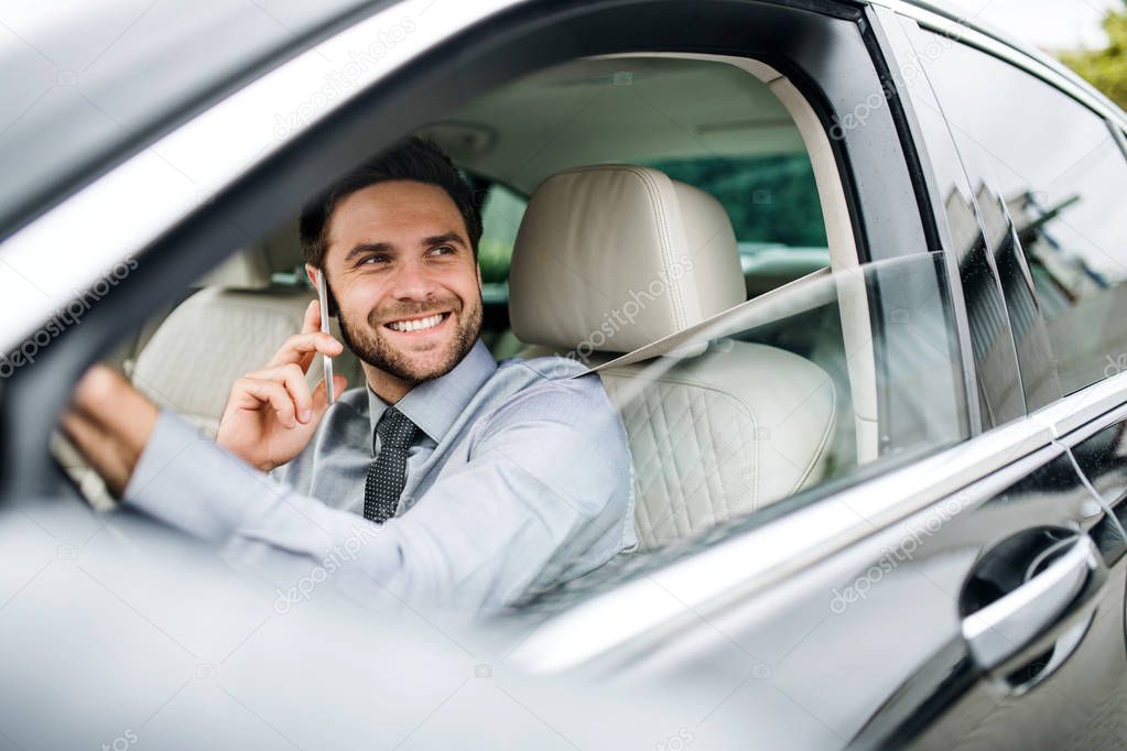 Young businessman with shirt, tie and smartphone sitting in car.