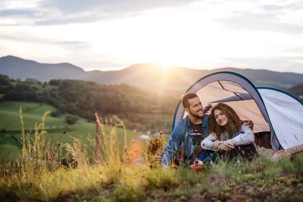 Young tourist couple travellers with tent shelter sitting in nature, drinking coffee. — Stock Photo, Image