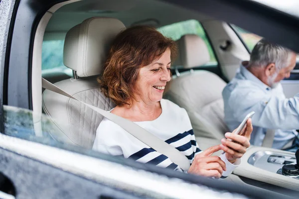 Feliz pareja de ancianos con teléfono inteligente sentado en el coche, va de viaje . — Foto de Stock