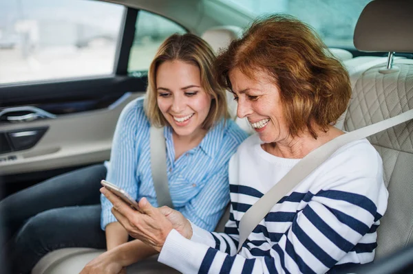 Adultos alegres sentados en los asientos traseros en el coche, utilizando el teléfono inteligente . — Foto de Stock