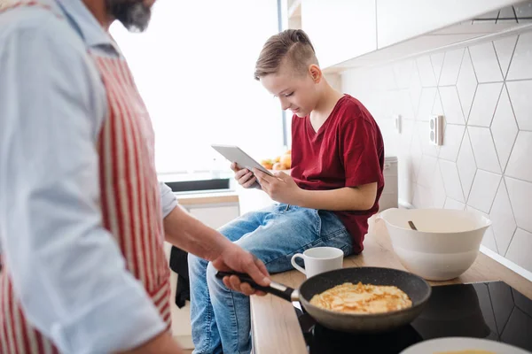 Padre maturo con piccolo figlio al chiuso in cucina, facendo frittelle . — Foto Stock