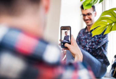 Akıllı telefonu olan genç arkadaşlar içeride oturup fotoğraf çekiyorlar. Ev paylaşımı konsepti.