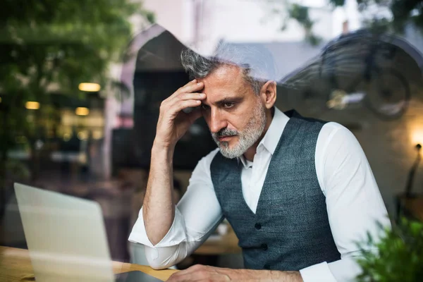 Ernster reifer Mann sitzt am Tisch in einem Café und benutzt Laptop. — Stockfoto