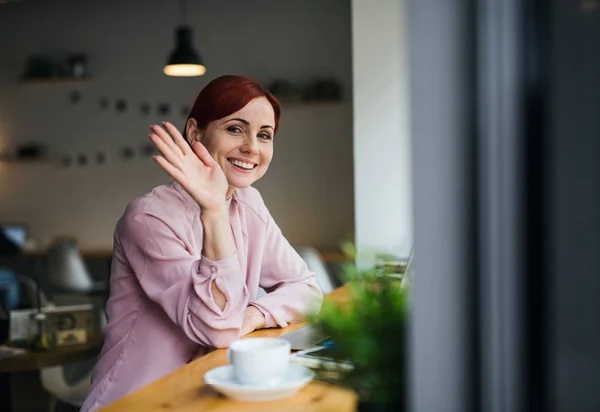 Un retrato de una mujer con café sentada a la mesa en un café, saludando . —  Fotos de Stock