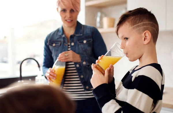 一个带着孩子在厨房里喝果汁的年轻女子. — 图库照片