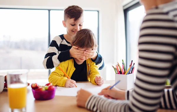 Een jonge vrouw met twee kinderen tekenen in een keuken. — Stockfoto