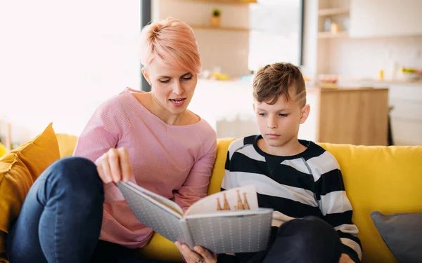 Uma jovem mulher com um filho dentro de casa, lendo um livro . — Fotografia de Stock