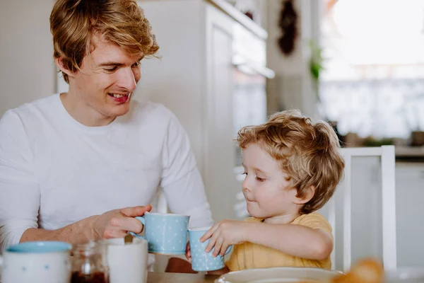 Giovane padre con un figlio bambino che fa colazione al chiuso a casa . — Foto Stock