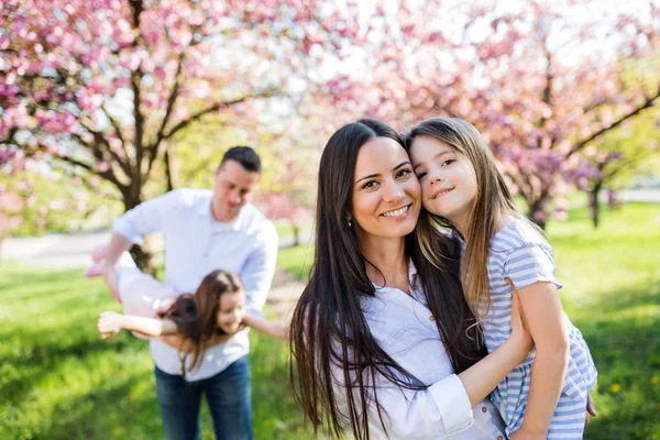 Mladí rodiče s malými dcerami stojící venku v jarní přírodě. — Stock fotografie