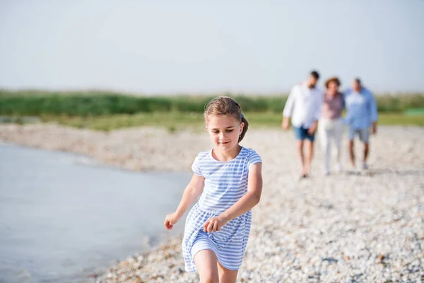 Piccola ragazza con la famiglia in vacanza passeggiando lungo il lago, tenendosi per mano . — Foto Stock