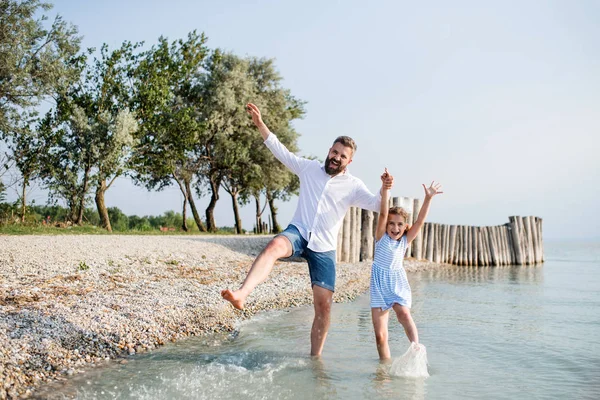 Dospělý otec a malá dcera na dovolené, kterou hrají u jezera. — Stock fotografie