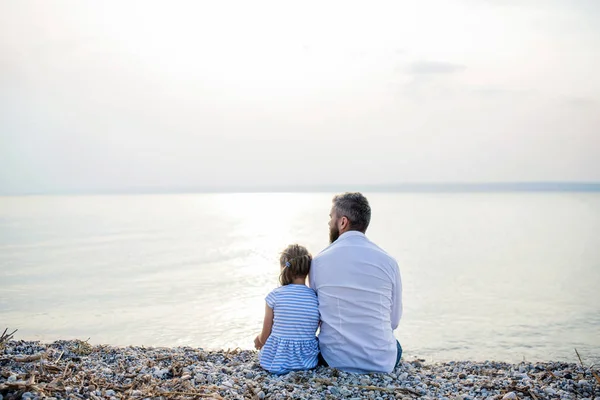 Vista trasera de padre e hija pequeña en un día de fiesta sentado junto al lago . —  Fotos de Stock
