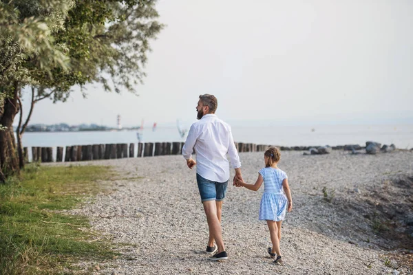 Vista posteriore del padre maturo che cammina con la piccola figlia in una vacanza al lago . — Foto Stock