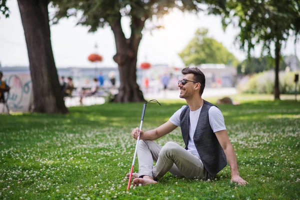 Junger Blinder mit Blindenstock und Blindenhund sitzt in Park in der Stadt. — Stockfoto