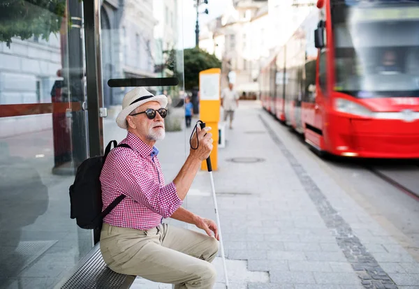 Starszy niewidomy mężczyzna z białą laską czeka na transport publiczny w mieście. — Zdjęcie stockowe