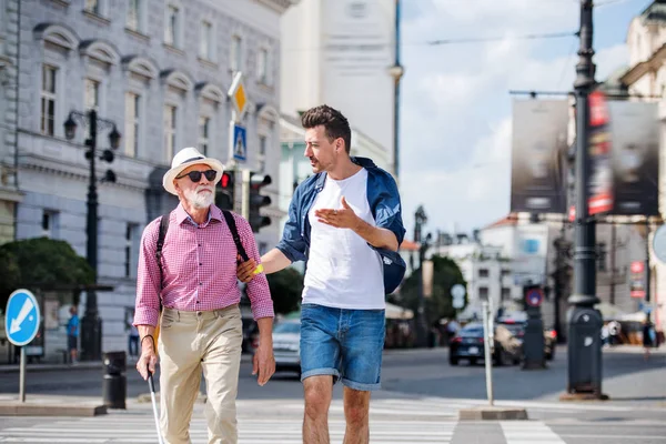 Jovem e cego sênior com cana branca andando na cidade, cruzando rua . — Fotografia de Stock