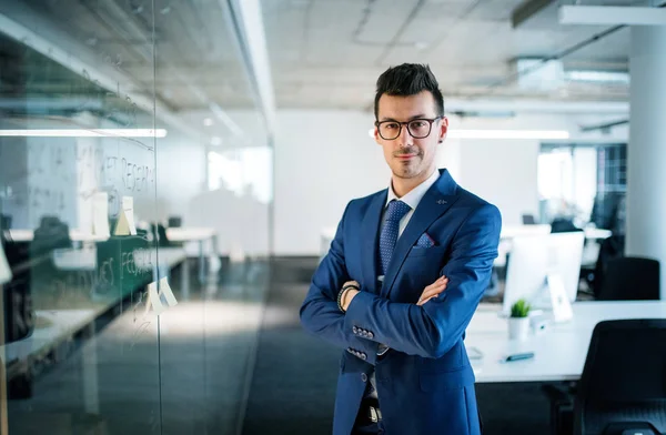 Portrait d'un jeune homme d'affaires debout dans un bureau, bras croisés . — Photo