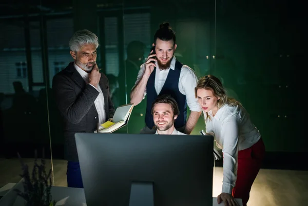 Een groep zakelijke mensen in een kantoor 's nachts, met behulp van computer. — Stockfoto