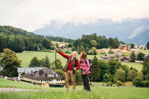 Oudere gepensioneerde echtpaar met nordic walking stokken wandelen in de natuur, praten. — Stockfoto