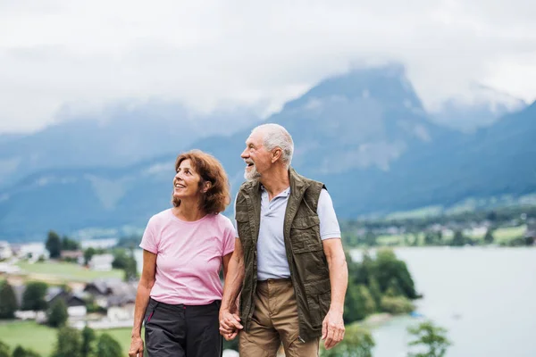 Starší důchodce pár pěší turistika v přírodě, držící se za ruce. — Stock fotografie