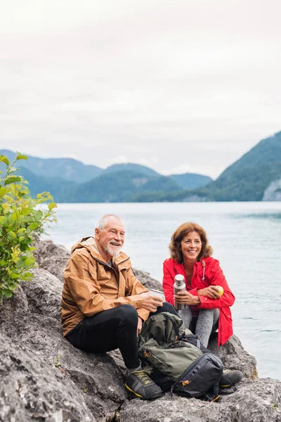 Un couple de pensionnés seniors marchant au bord du lac dans la nature, assis et se reposant . — Photo