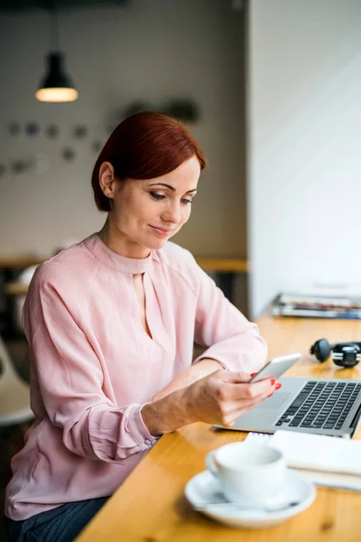 Una mujer con café sentada a la mesa en un café, usando un smartphone . — Foto de Stock