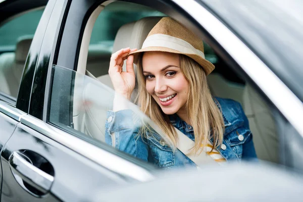 Junge Frau mit Hut sitzt im Auto und schaut hinaus. — Stockfoto