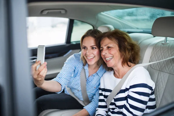 Adultes joyeux avec smartphone assis sur les sièges arrière dans la voiture, prendre selfie . — Photo