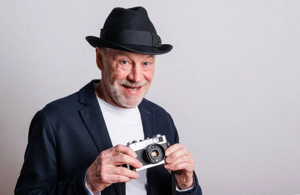 Portrait of a senior man with hat and camera in a studio. — Stock Photo, Image